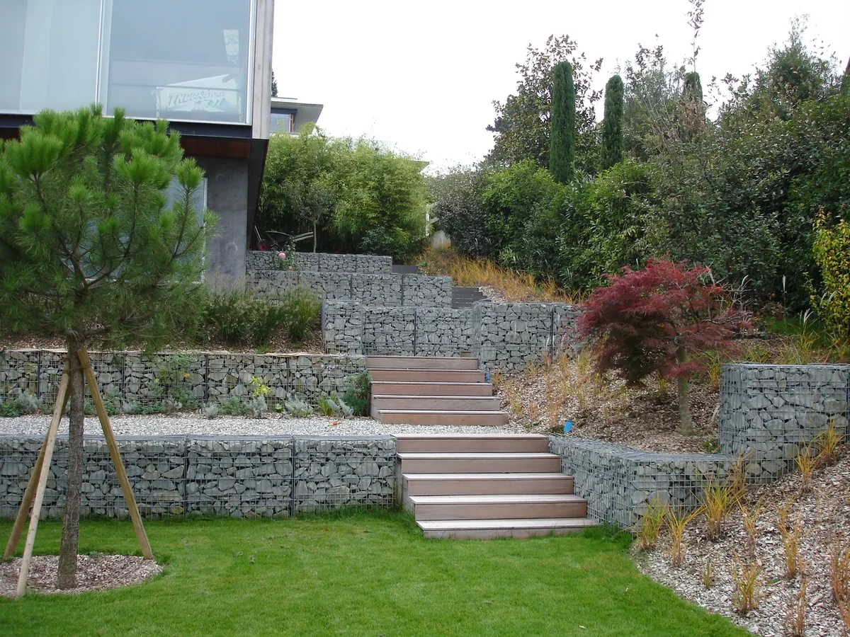 Terrassierter Hanggarten mit mehreren Gabionen-Ebenen und Holztreppe